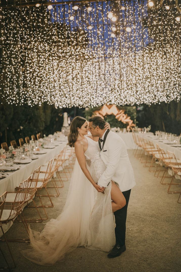 Fair light canopy with the bride in sparkly wedding dress and groom in white tuxedo for destination wedding 