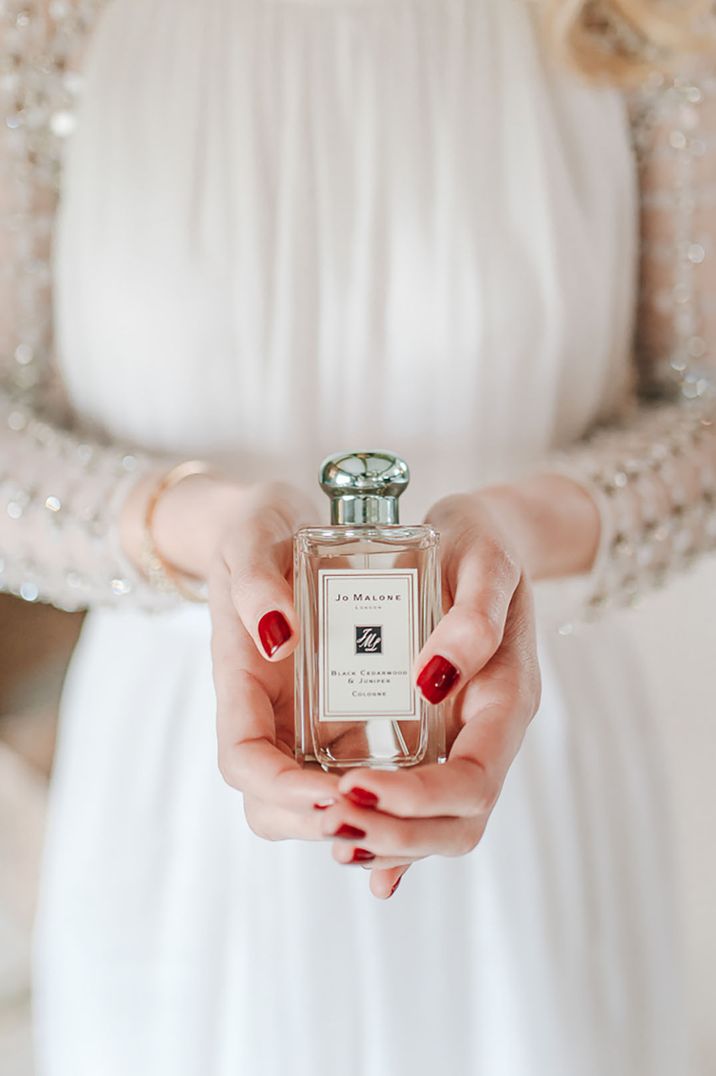 Bride with red painted wedding nails holding bottle of Jo Malone London wedding cologne 