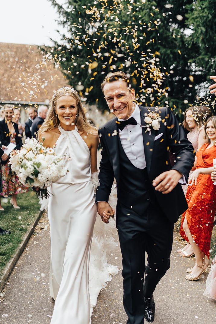 Bride in halter neck wedding dress with feathers having confetti moment with the groom in black tuxedo 