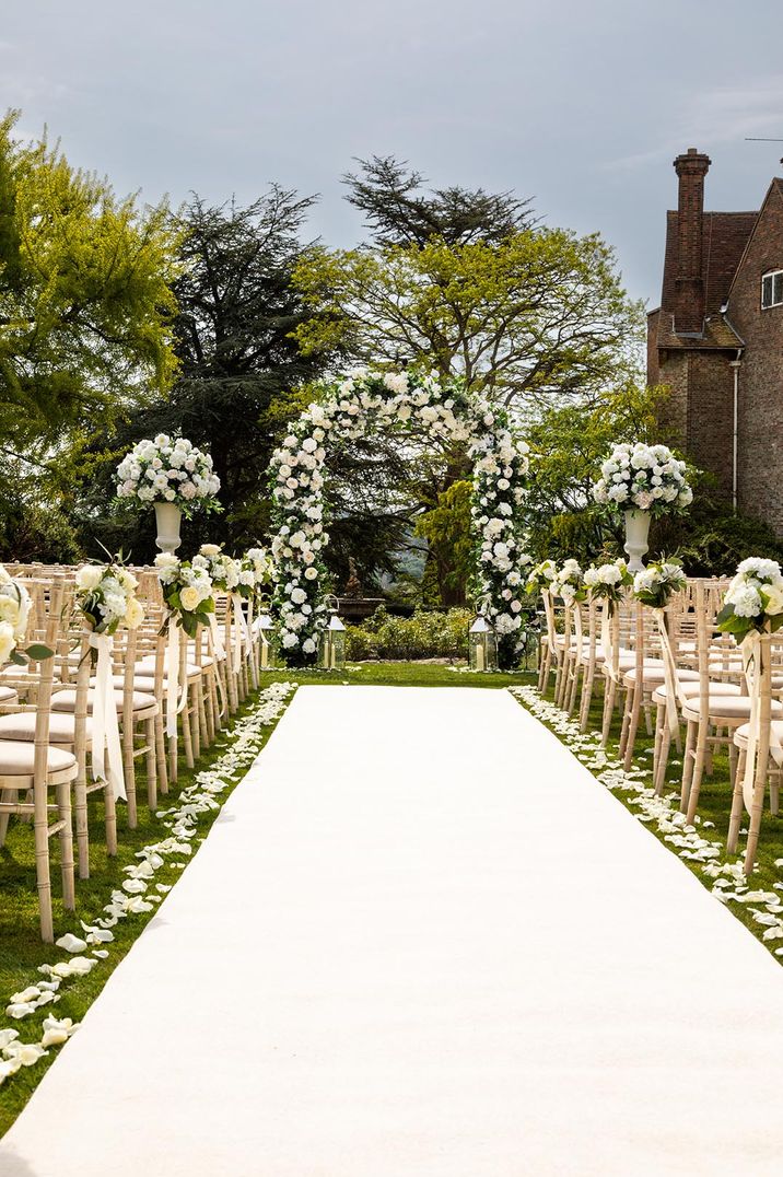 Outdoor wedding ceremony at Farnham Castle with white aisle carpet with white rose petals and flower arch altar decor 