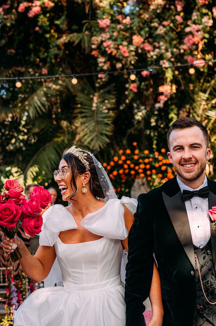 Bride wearing a bow wedding dress carrying a pink rose wedding bouquet with groom in tuxedo 