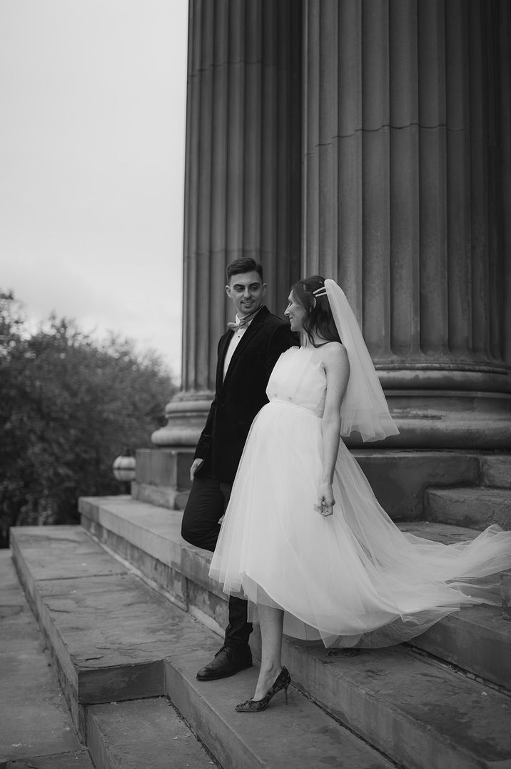 Pregnant bride wearing a tulle wedding dress walking with the groom 