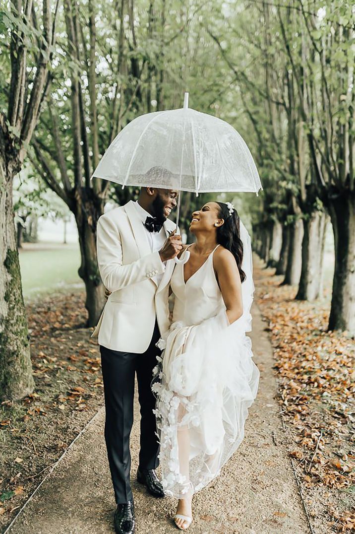 Coworth Park wedding with the bride and groom in their white wedding outfit under clear umbrella 