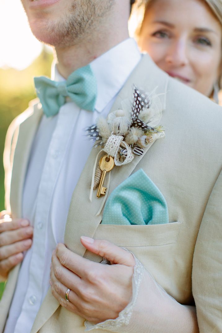 Groom in a stone suit with turquoise bow tie and pocket square and a feather and key buttonhole