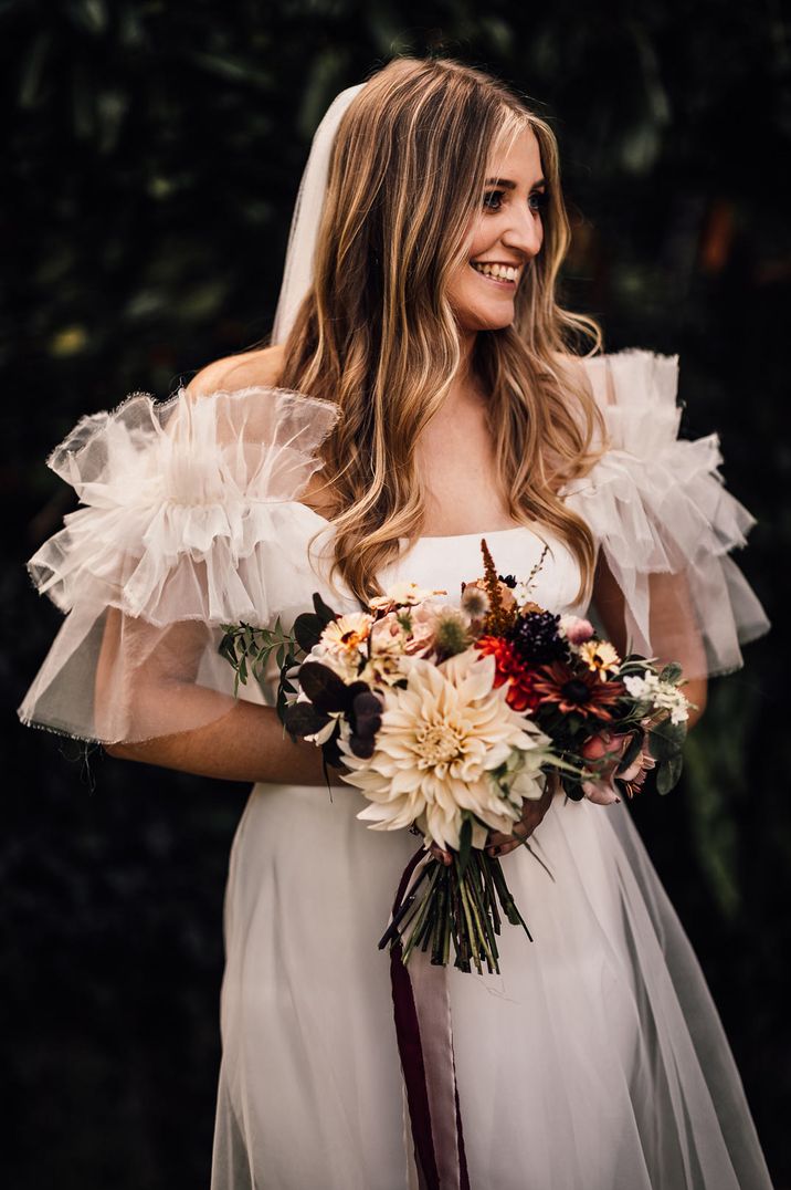 Bride in off the shoulder ruffled dress with floral bouquet 