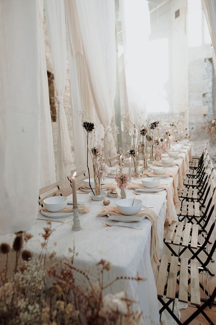 White, peach and pink wedding table setting with wooden chairs and drapery 