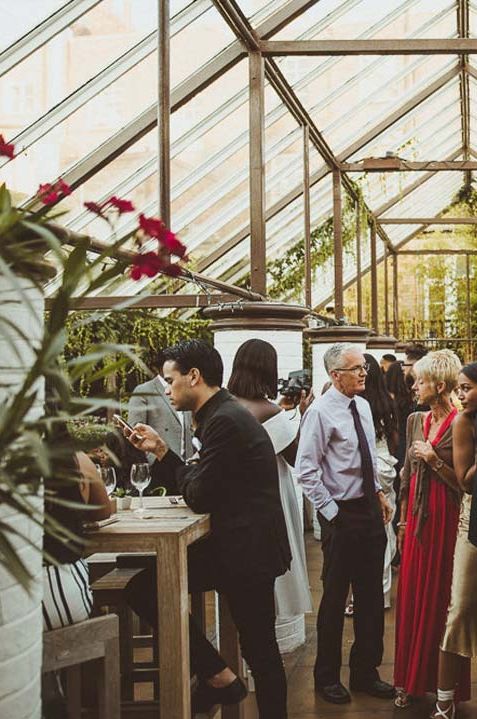 Guests mingling under domed roof of Clifton Nurseries London glasshouse wedding venue 