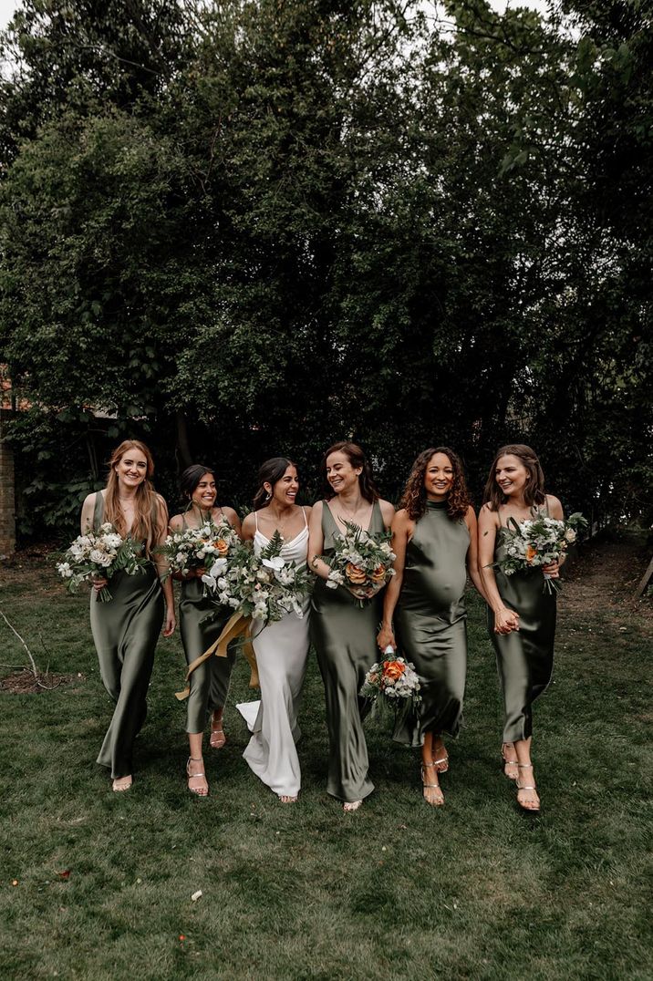 Bridesmaids in mismatched satin green bridesmaid dresses with the bride in a satin slip wedding dress 