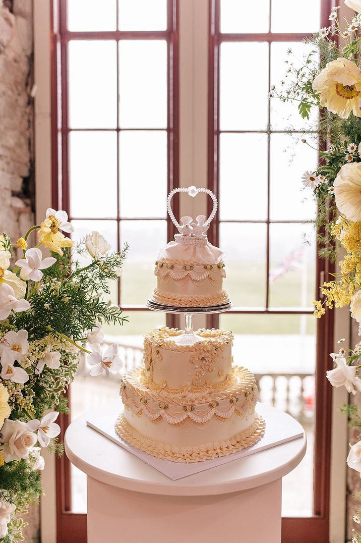 Castle wedding with luxury heart shaped vintage wedding cake with pastel yellow and white frosting with dove cake topper 