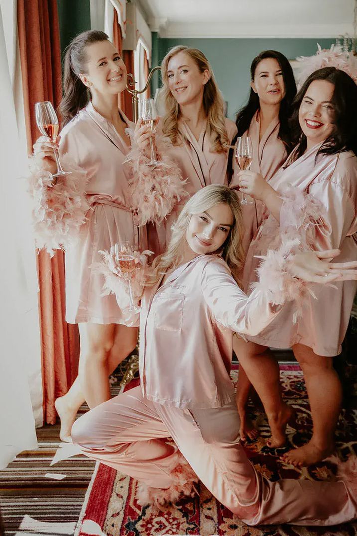 Bridal party posing in pale pink satin pyjamas with feather trims by The Kensington Photographer