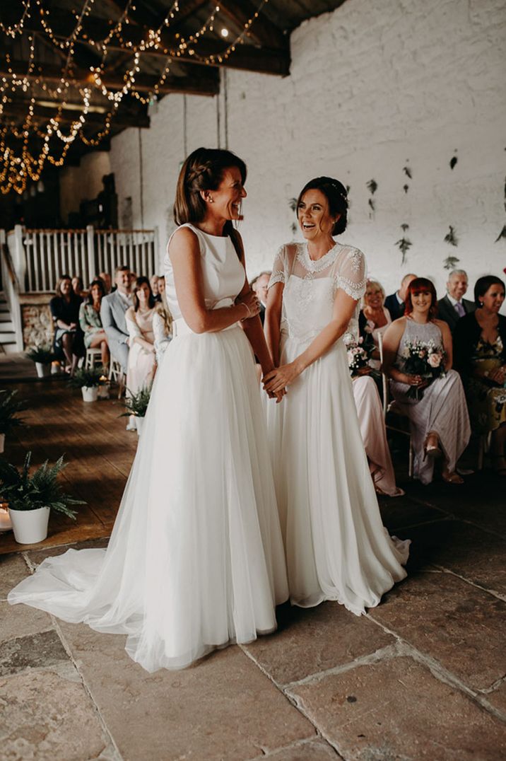 Two brides at the alter of a civil wedding ceremony with fairy light ceiling decorations holding hands