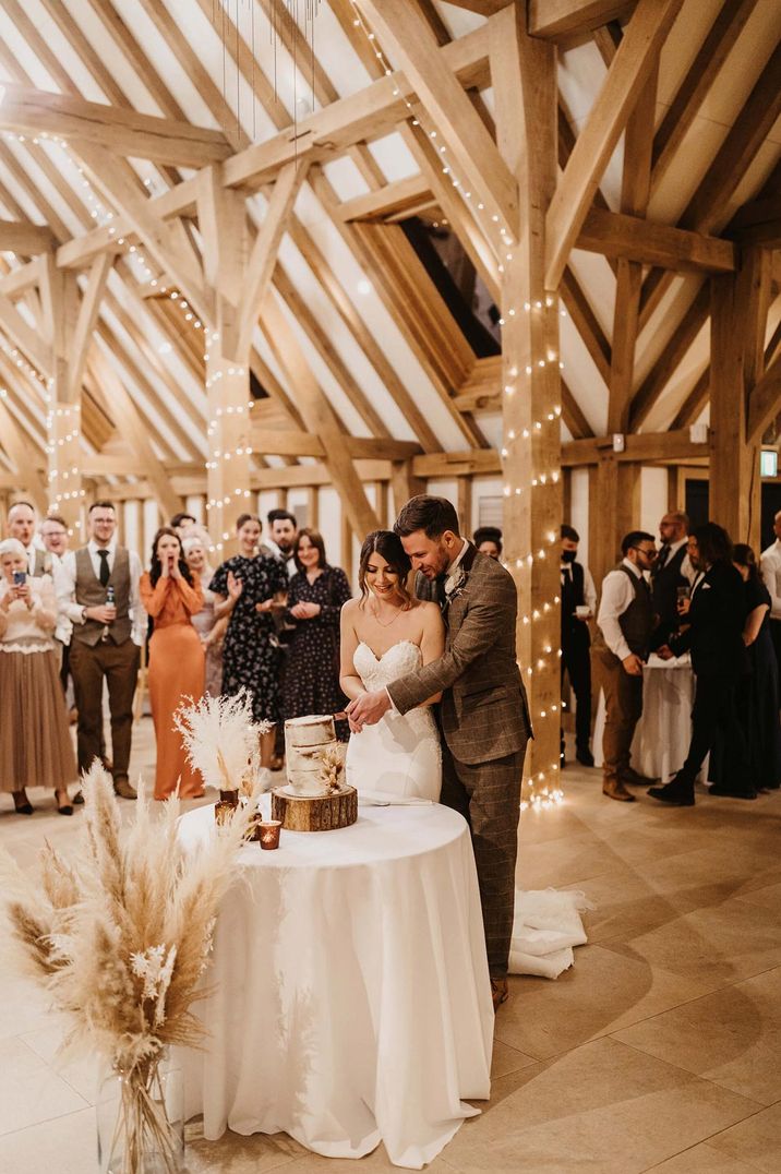 Bride in strapless sweetheart neckline wedding dress and groom in brown checkered suit cutting three tiered buttercream wedding cake