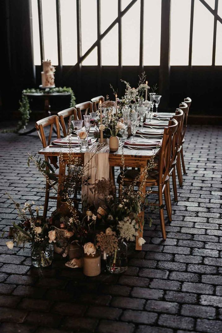 Rustic luxe wedding tablescape with a variety of dried flower and rose flower arrangements in vases, tapered candles, sheer tulle table runner at Elmley Nature Reserve wedding venue search 