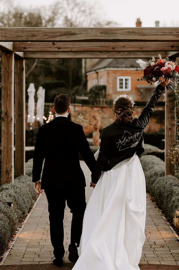 Bride wearing leather jacket walking along with the groom at Syrencot wedding venue 