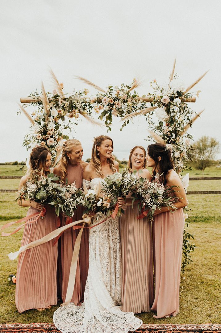 Bridal party in pink bridesmaid dresses pose with bride at outdoor wedding 