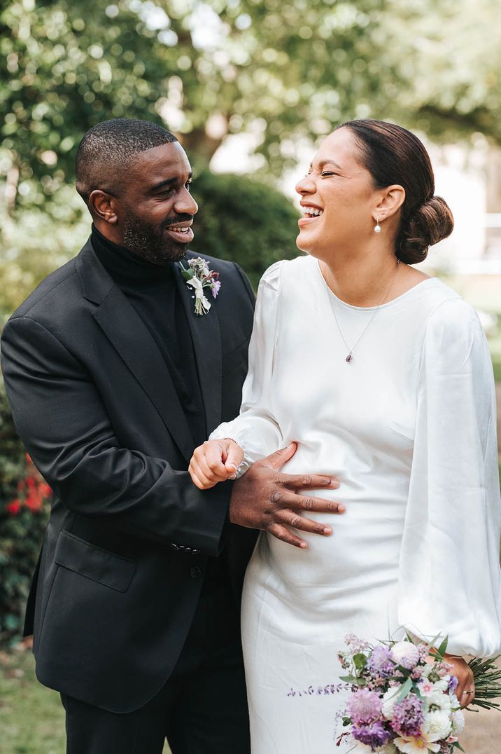 Groom wearing all black places his hand on the bride's baby bump 