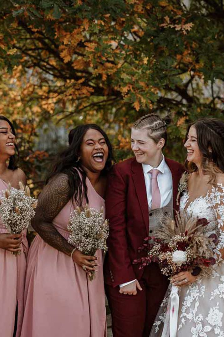 Dusky pink bridesmaid dresses with two brides in illusion lace wedding dress and a burgundy suit 