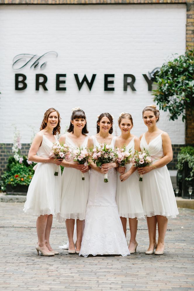 Bridal party wearing short white bridesmaid dresses and pink neutral floral bouquets