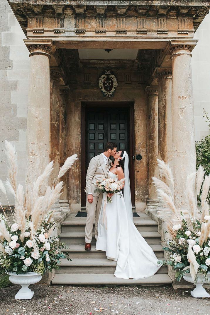 Bride and groom embracing on the steps of Elmore Court with pampas grass floral arrangements