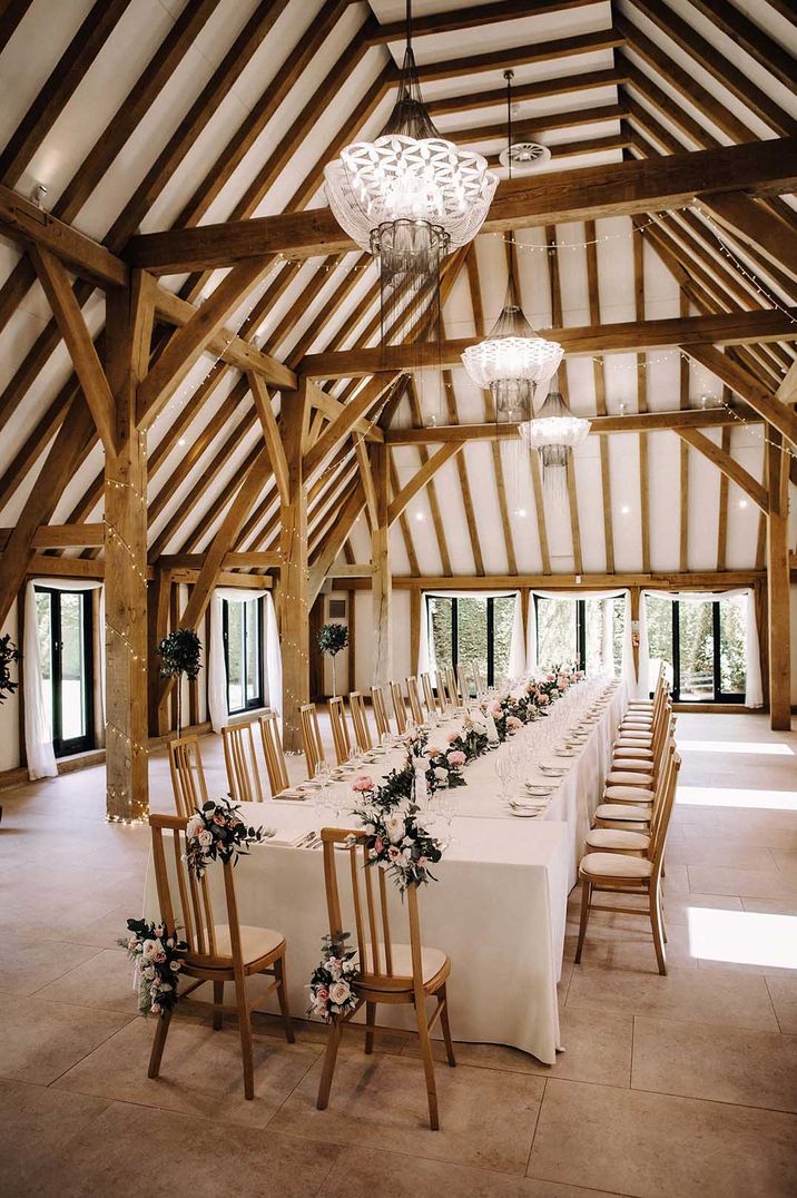 Large long wedding table with white neutral tablescape and rose decorations at barn wedding venue