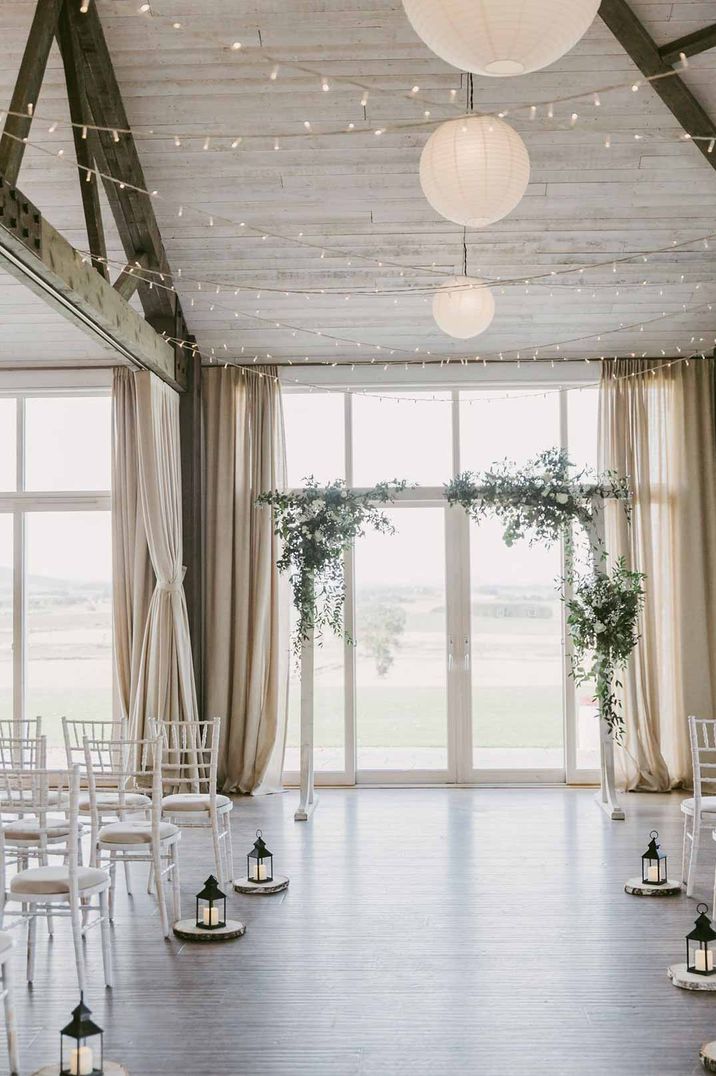 Wedding reception room of Barra Castle wedding venue Scotland with fairy lights, white wooden wedding arch, foliage arrangements and aisle candles 