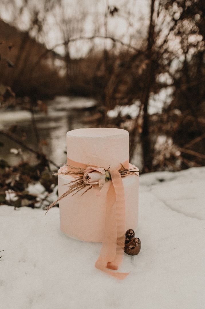 Two tier pale pink wedding cake set on table at outdoor snowy winter wedding 