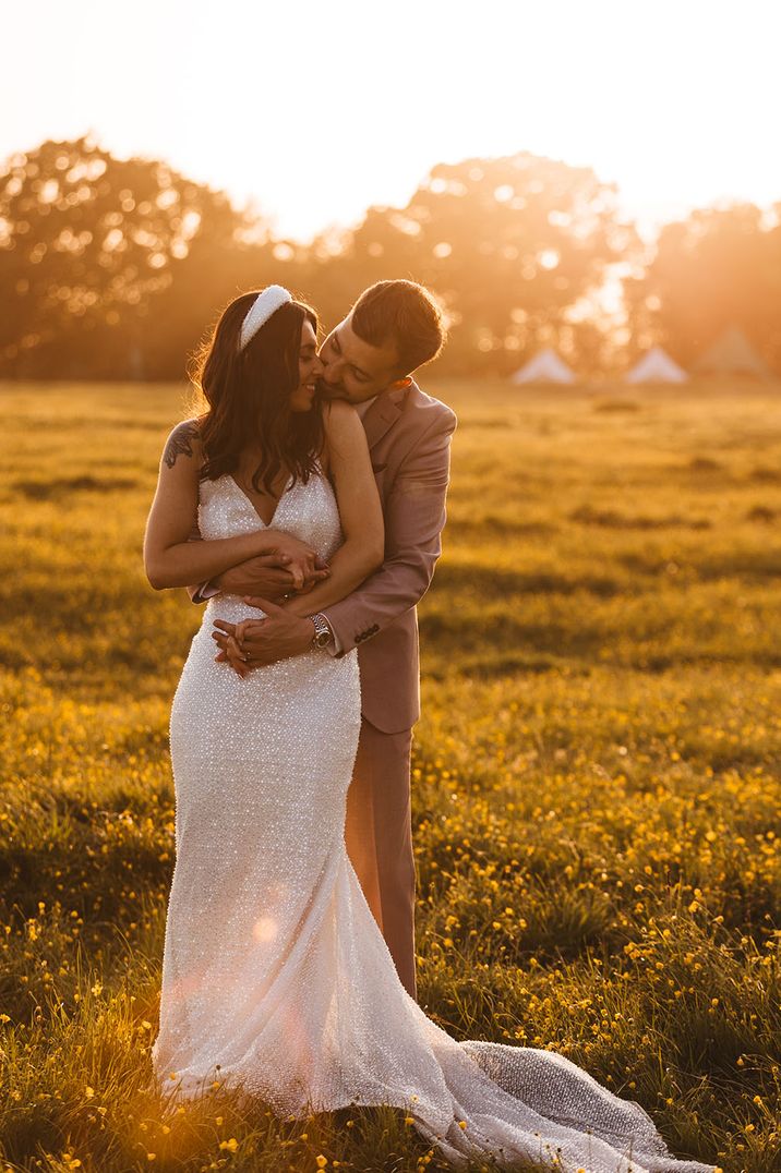 The groom embraces the bride from behind as they pose together for couple portraits in the sunset 