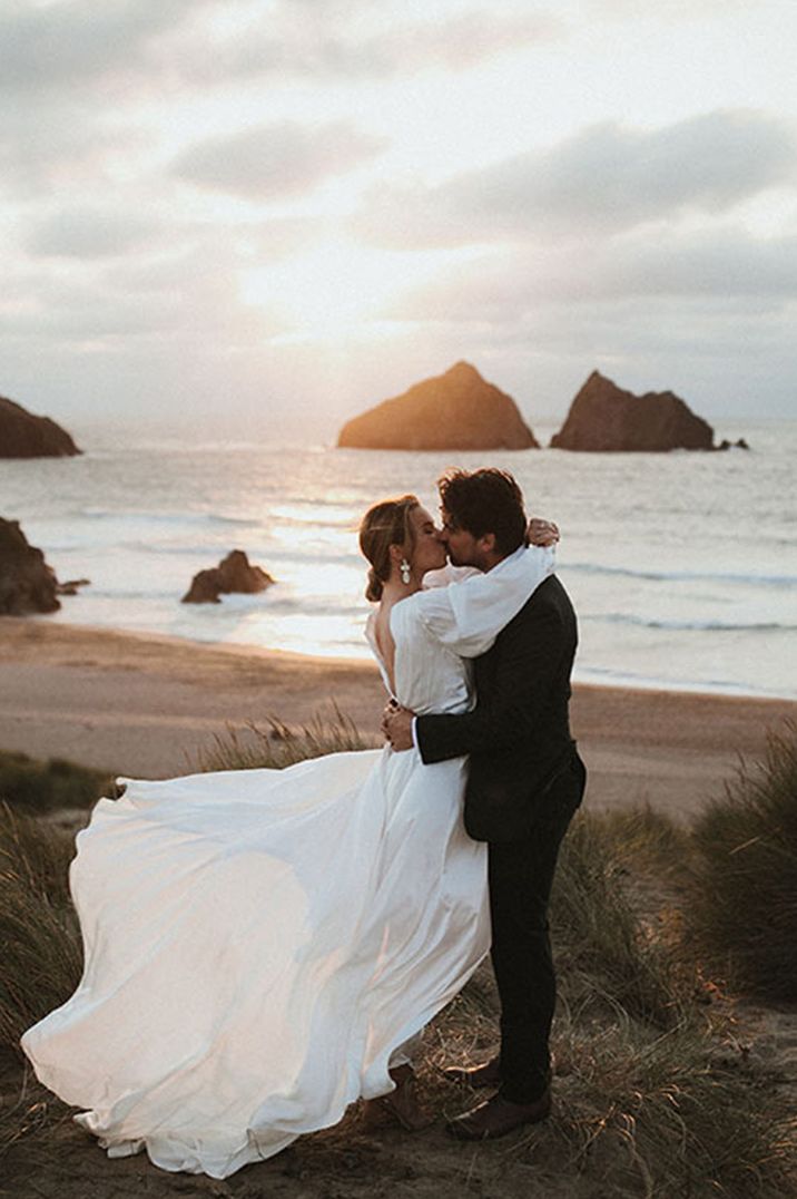 Golden hour couple portrait with bride in floaty wedding dress embracing the groom on the beach 