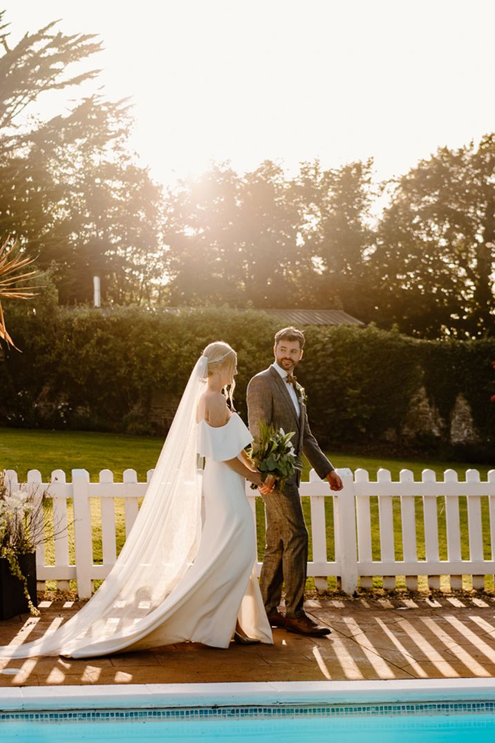 Golden hour couple portrait with bride wearing off the shoulder wedding dress with brown tweed suit 