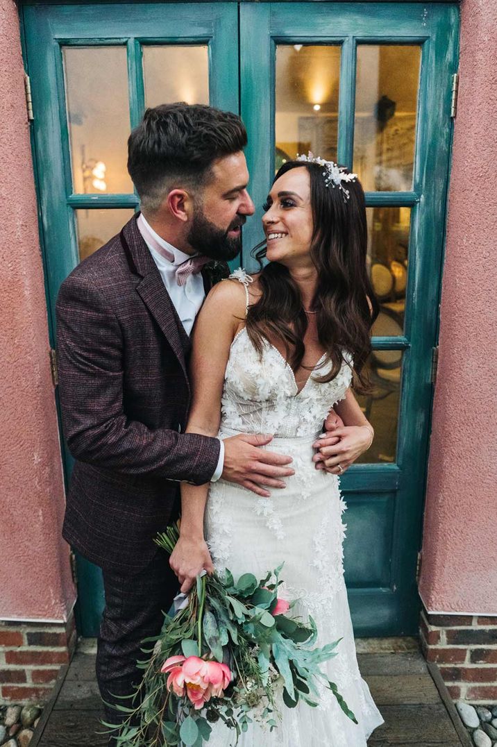 Groom in stylish tweed suit and bride in V neck strappy wedding dress embracing at Le Petit Chateau