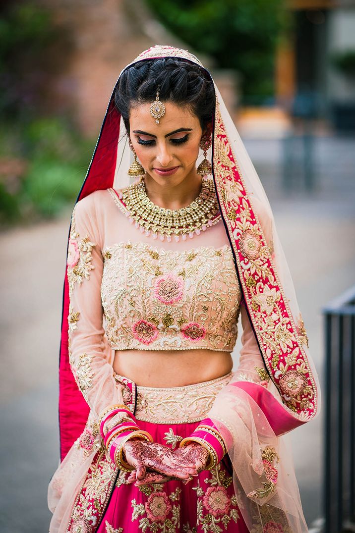 Bride in pink lehenga who gold detailing for Hindu fusion wedding with traditional henna 