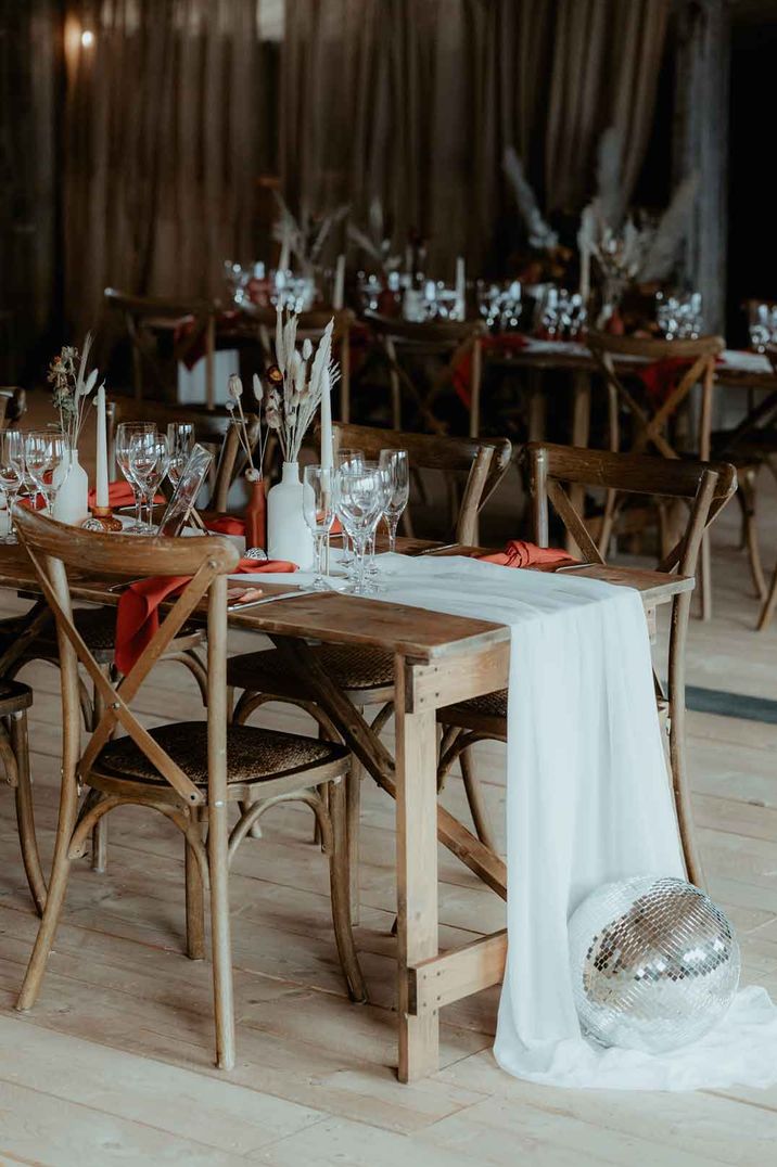 Rustic luxe wedding tablescape at Rhyse Farm wedding venue - white table runners, orange wedding napkins, pampas grass in white ceramic vases, dried flower centrepieces and disco ball wedding decor 