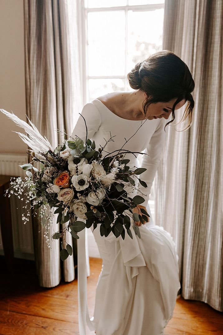 Bride carrying large oversized wedding bouquet with anemones, roses and pampas grass 