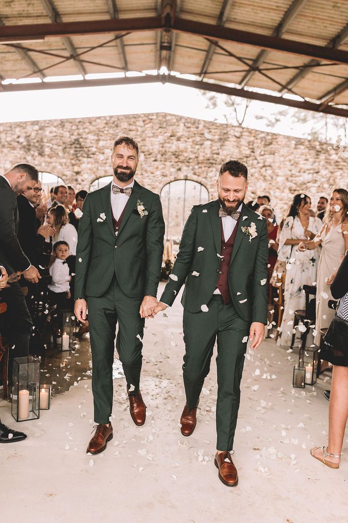 Secular wedding ceremony at gay wedding with two grooms in dark green suits with boho styling 