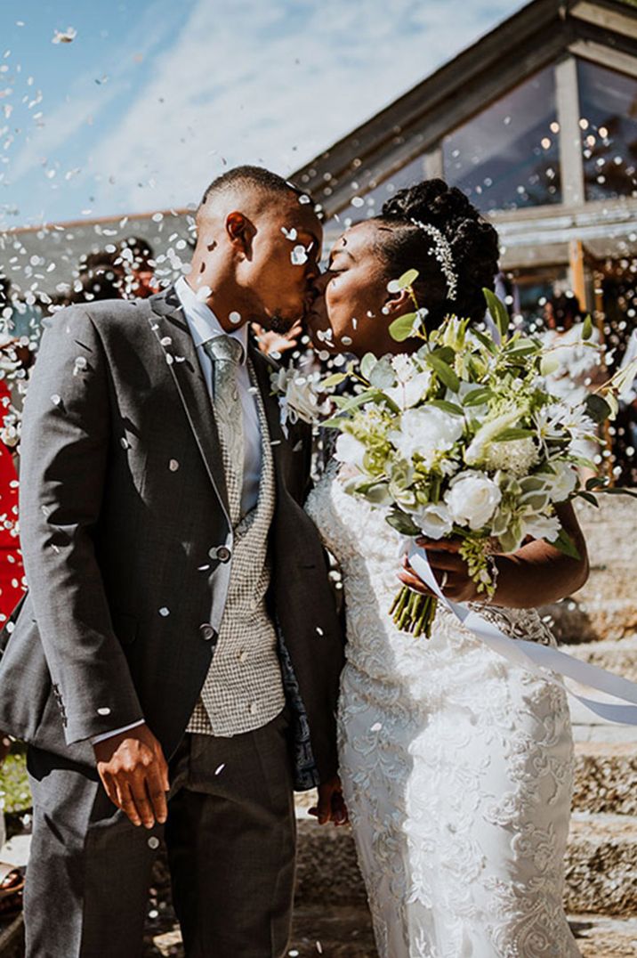 Bride in traditional lace wedding dress kissing the groom for their confetti exit 