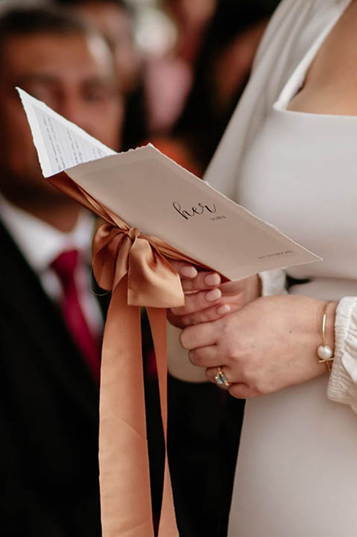 Orange satin bow holding the wedding vow booklet together 