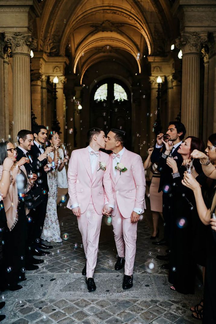 Two grooms wearing light pink wedding suits as they have a confetti moment protected by wedding insurance 