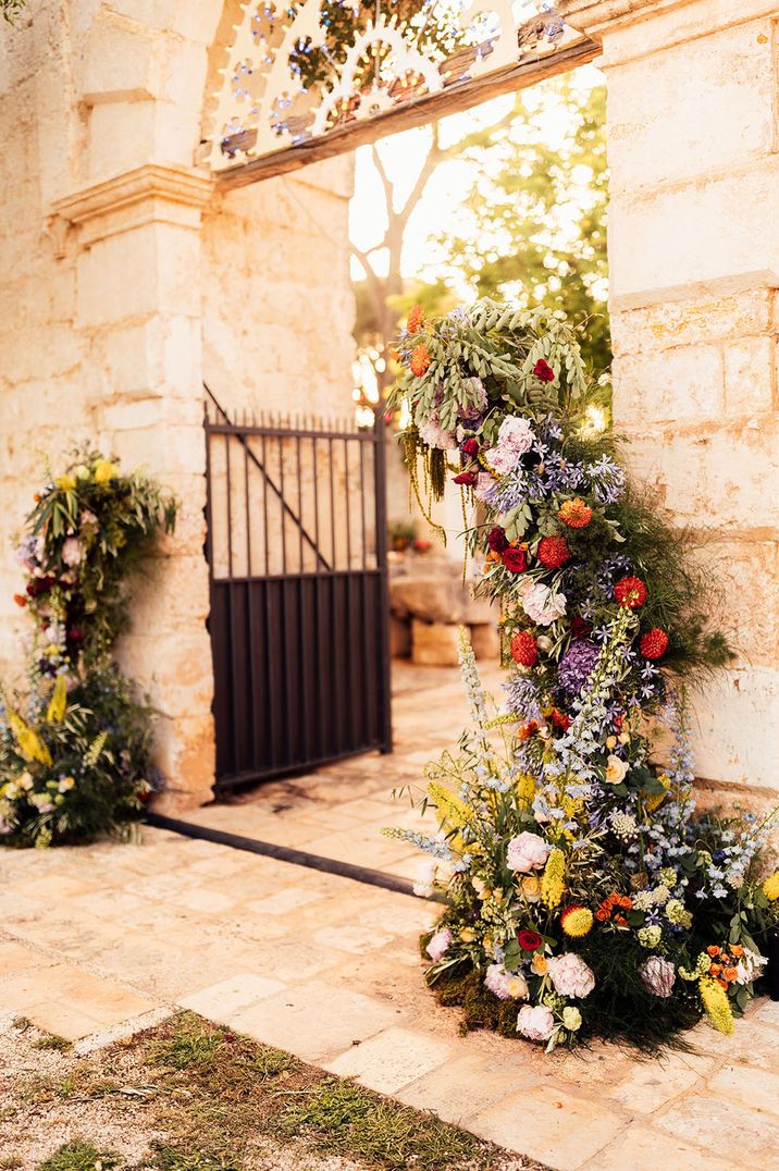 Destination wedding in Puglia, Italy with bright colourful wedding flower columns in shades of red, pink, and purple colours 