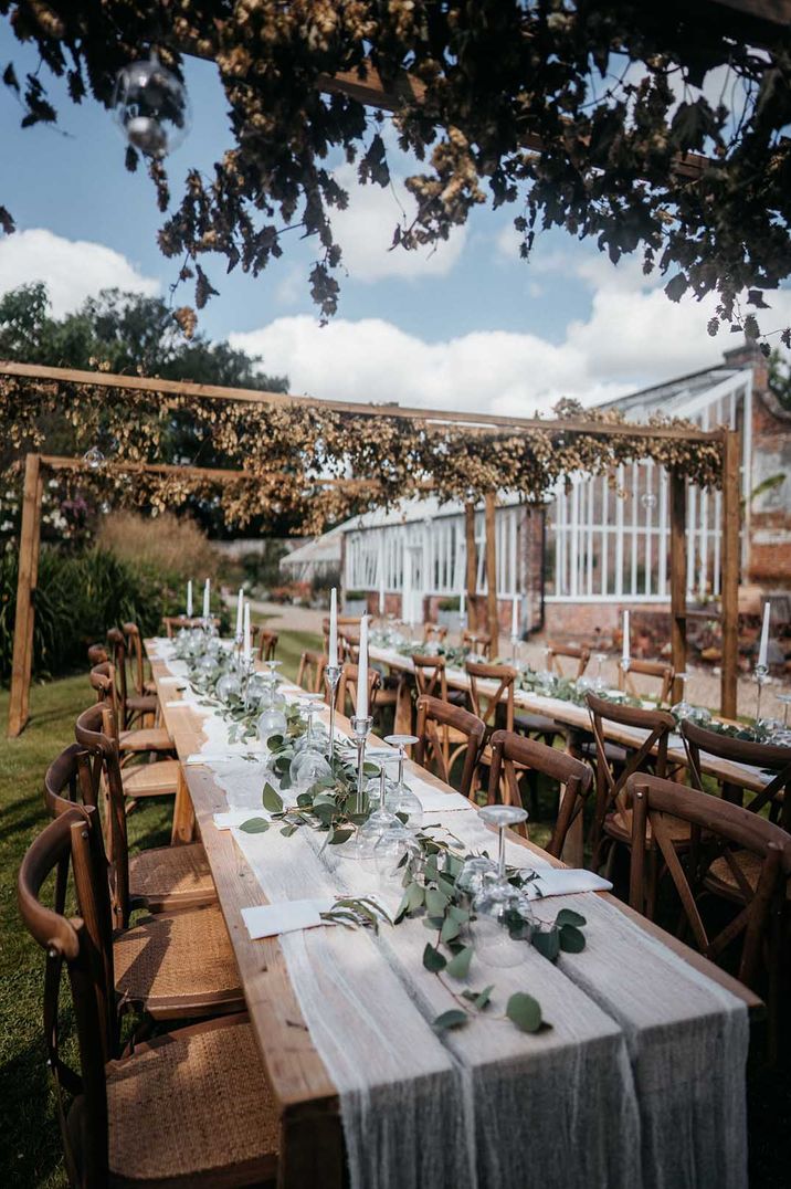 Outdoor summer wedding ceremony at Wasing Park with sheer white table runners, eucalyptus table runners, white tapered candles and wooden geometric decor with summer-toned floral decor 