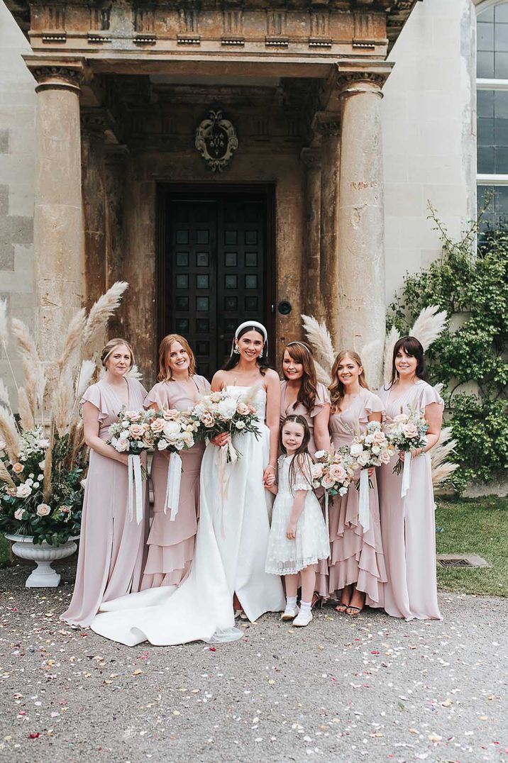 Bride in strappy satin wedding dress with puddle train standing with bridesmaids in ruffle short sleeve pink bridesmaid dresses 