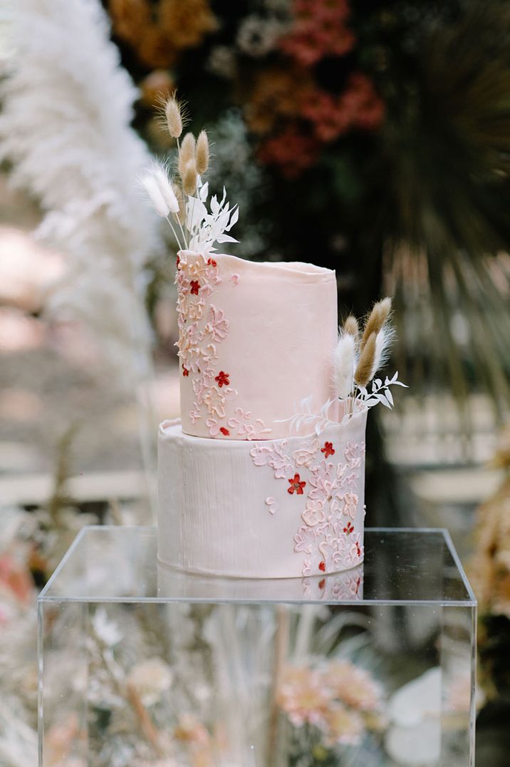 Two tier pink iced wedding cake with iced flower design with white and neutral bunny grass decor for woodland wedding 