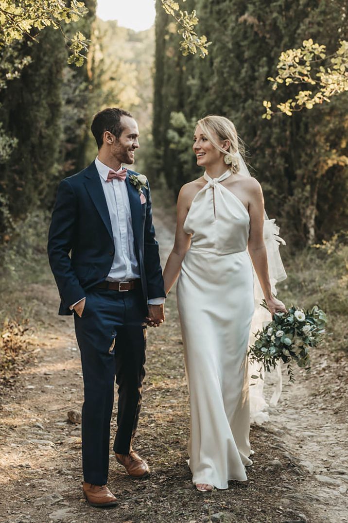 Groom in navy suit with pink bow tie with the bride in a satin halter neck wedding dress 