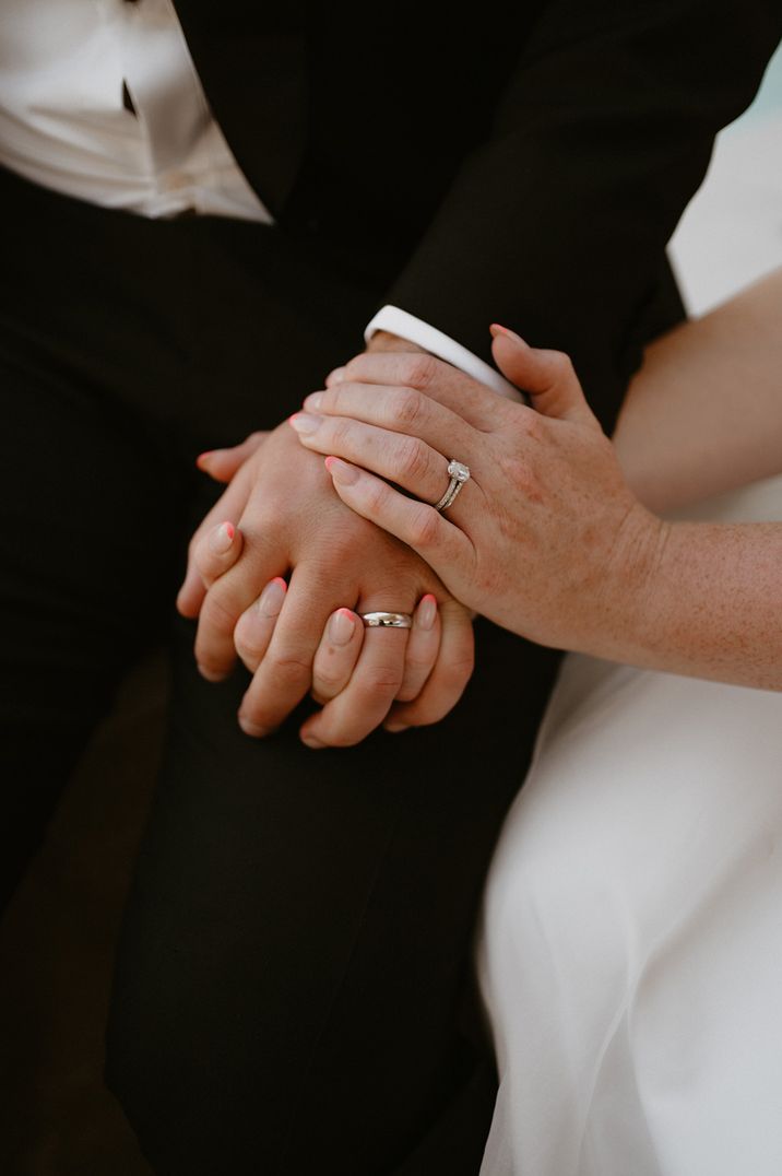 Bride and groom interlocking fingers on their wedding day showing off their new wedding bands 