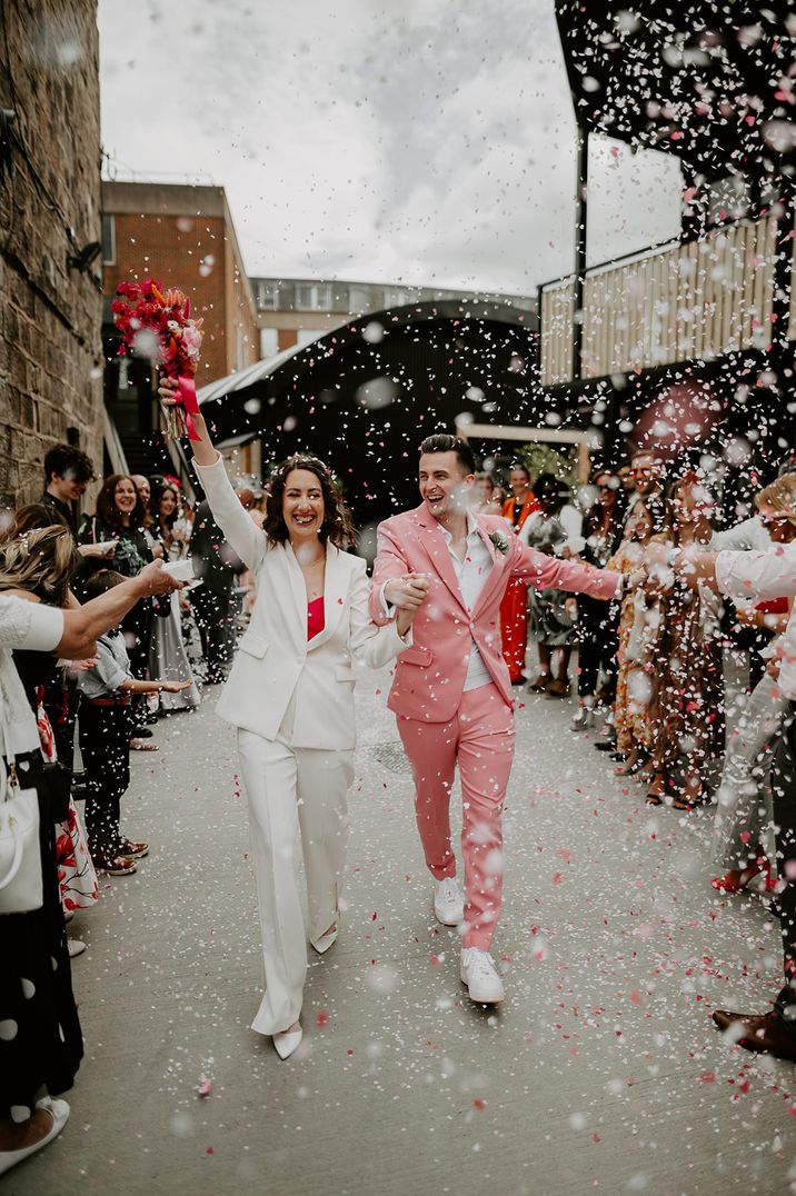 Epic confetti moment for grom in pink wedding suit and bride in white wedding suit