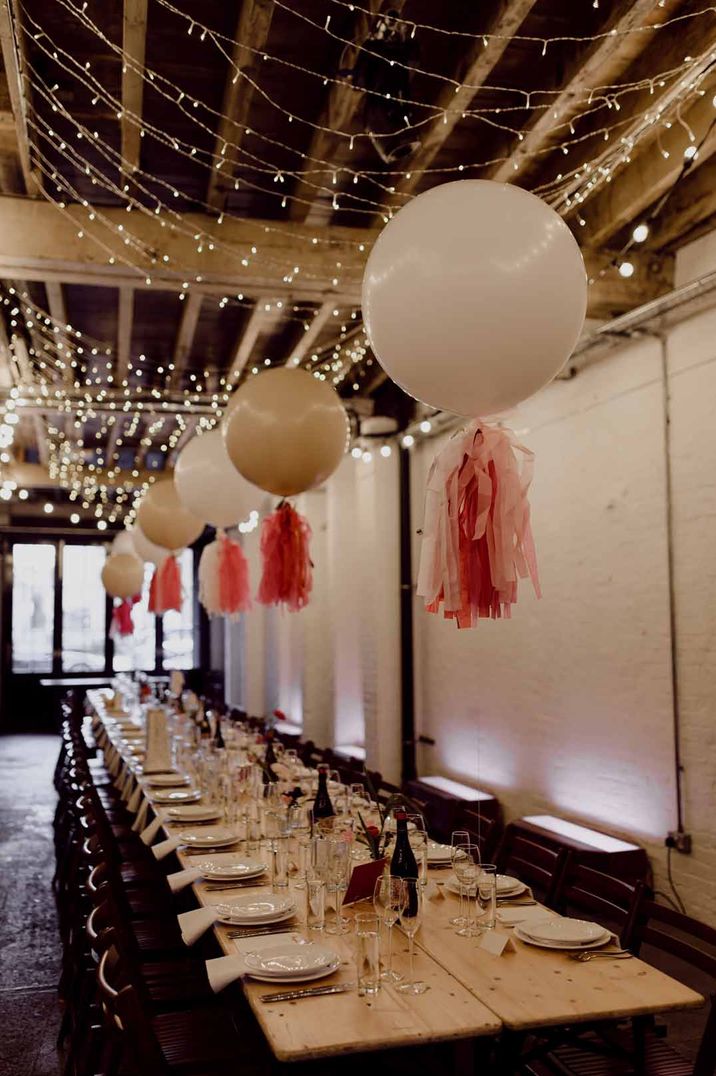 reception room of 100 Barrington London wedding venue - fairy lights, balloon wedding decor, hot pink and baby pink tassels and neutral wedding tablescape 