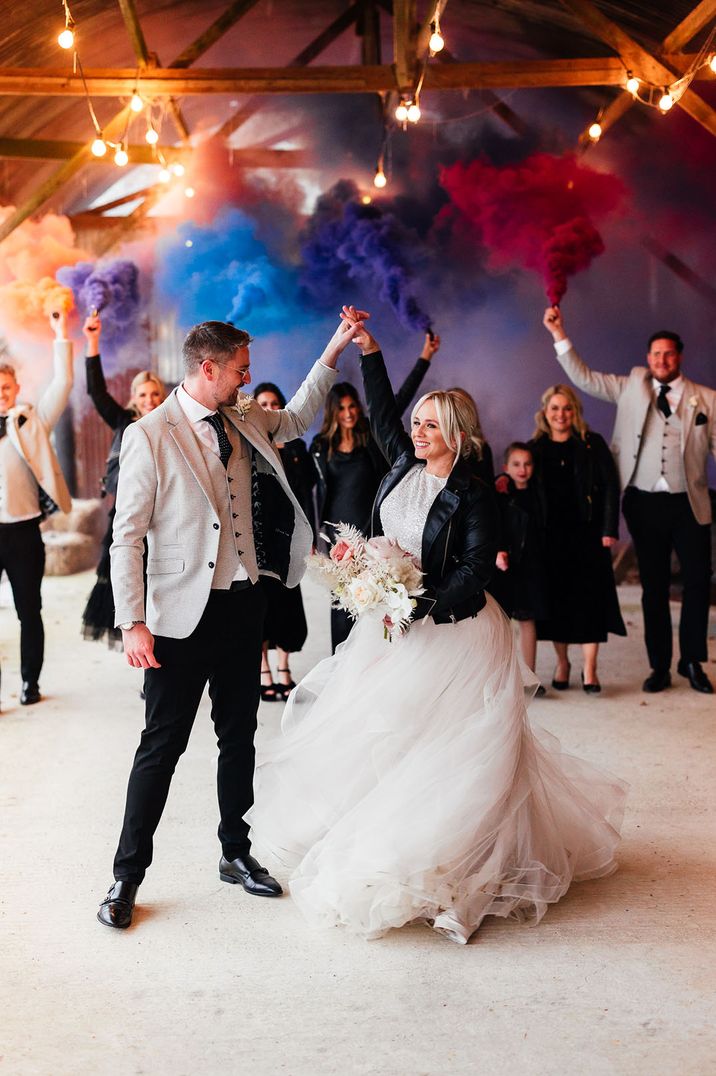 Bride in tulle bridal separates with black leather jacket with the groom and colourful smoke bomb flares 