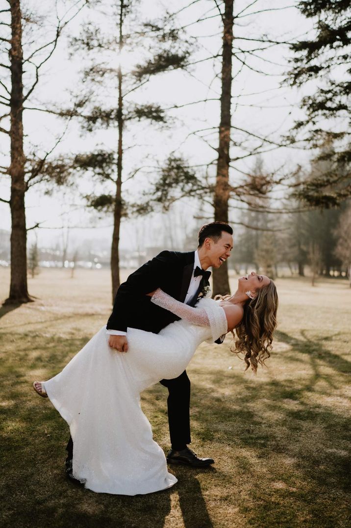 First look wedding photographs with groom in tuxedo leaning his bride in an off the shoulder Eva Lendel sparkly wedding dress over for a kiss