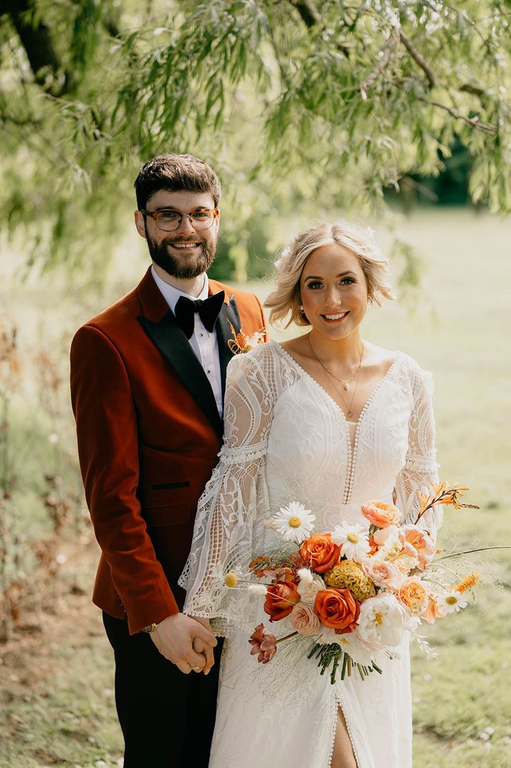 Bride in long bell sleeve wedding dress with groom in velvet suit jacket posing for couple portrait 