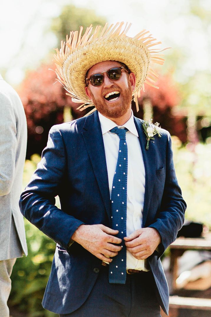 Man in dark navy blue suit with straw hat and black sunglasses enjoying the stag party 