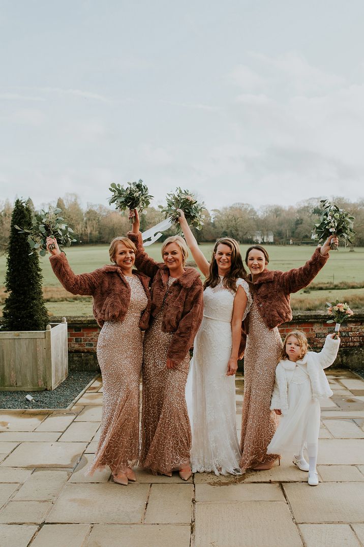 Bridesmaids in fitted gold sparkly bridesmaid dresses with faux fur coverups